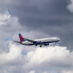 A Delta Air Lines airplane flying through a cloudy sky, with its landing gear extended, appearing to approach for landing.