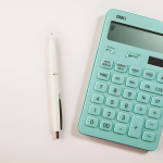 A teal calculator and white pen on a white surface.