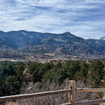 Snow-capped Rocky Mountains in Colorado seen from a wooden fence overlook.