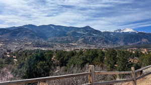Snow-capped Rocky Mountains in Colorado seen from a wooden fence overlook.