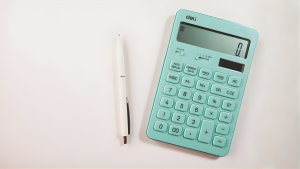 A teal calculator and white pen on a white surface.