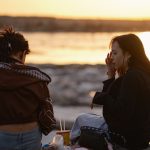 Two women sitting by the water at sunset