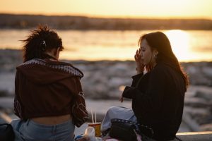 Two women sitting by the water at sunset