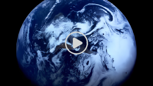 Planet Earth visible as a whole blue marble with white cloud swirls against the black background of space, taken from a video screen.